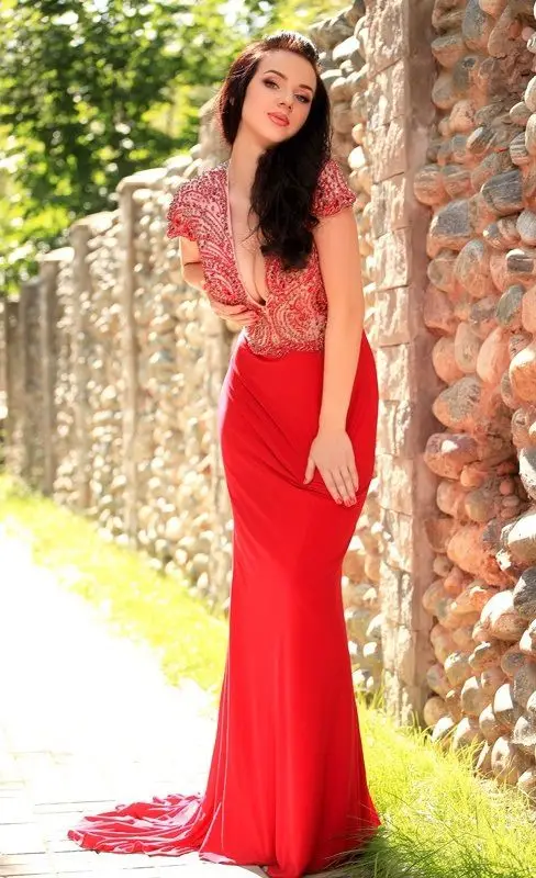 Iris in long red dress, posing near stone wall