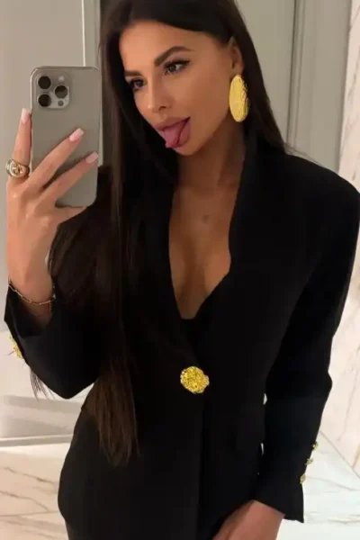 Escort Daniela in Amsterdam, wearing a cream blouse, teasing with cleavage.