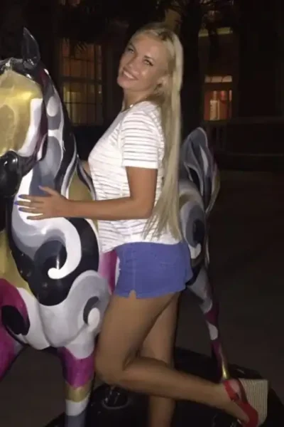 Lucy, a stunning blonde escort in Amsterdam, is wearing a revealing outfit and posing confidently.