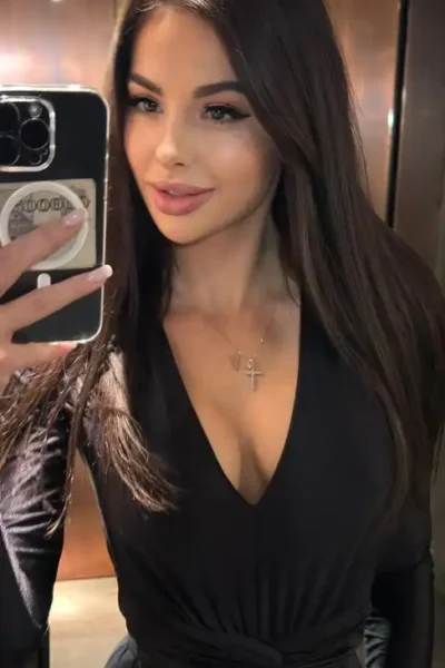 Daniela, a sexy Amsterdam escort in a low-cut black dress, looks confident.