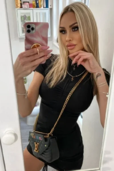 Blonde escort Meredith wearing black dress and handbag selfie
